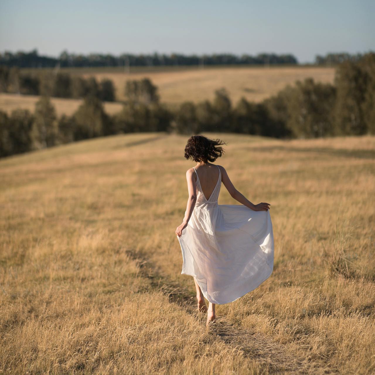 Femme en robe blanche marchant pieds nus dans un champ, symbole de liberté et fertilité